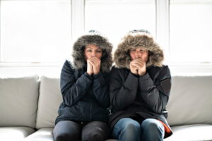 man-and-woman-wearing-parkas-with-hoods-on-sit-on-couch
