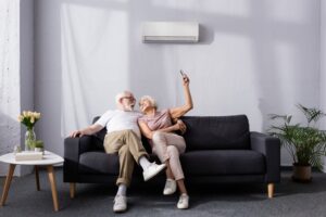 senior-couple-sitting-on-couch-turning-on-mini-split-with-remote